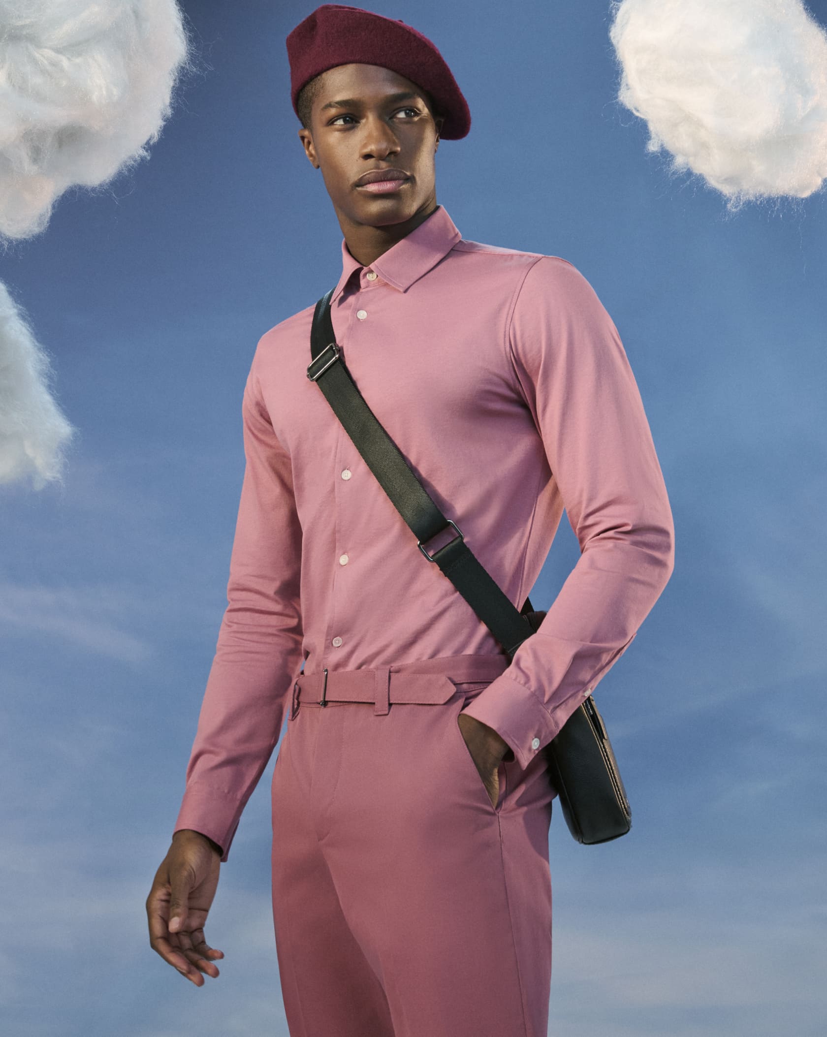 Man in a hat wearing a pink shirt and pink trousers with a cross body bag