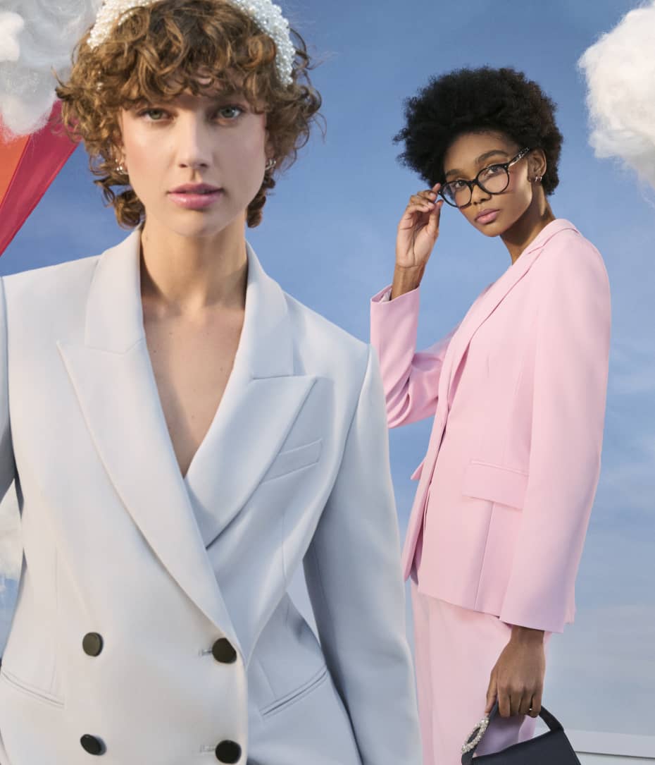Two women, one wearing a blue blazer and woman behind wearing pink co ord suit