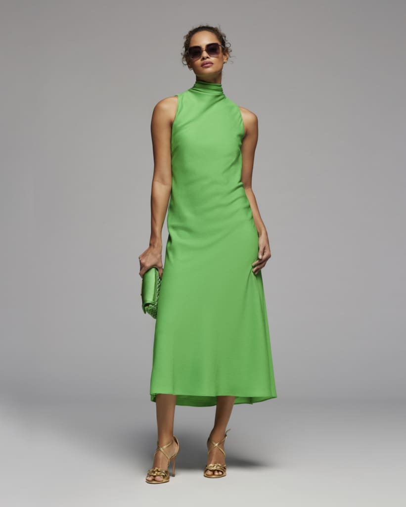 Woman in a green dress wearing sunglasses and holding a green clutch