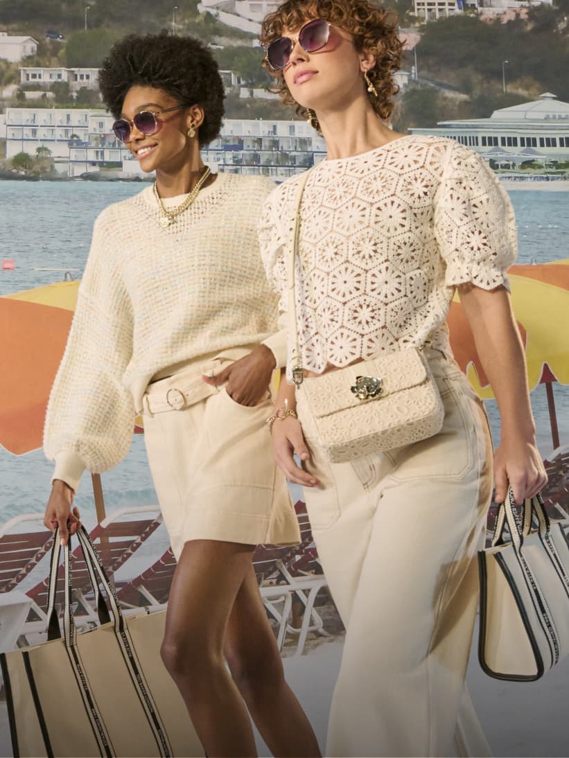 Two women wearing white tops and white bottoms carrying ecru handbags