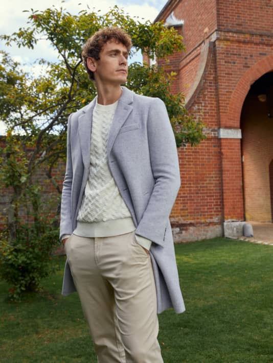 Man in light grey wool coat with cream jumper underneath