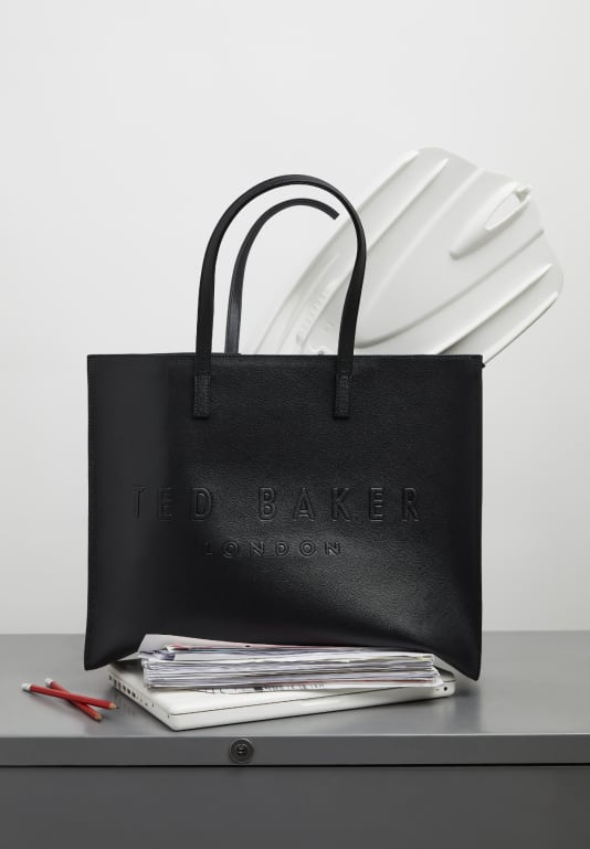 Women's black tote bag on a desk with paperwork underneath and with a white flipper coming out of it