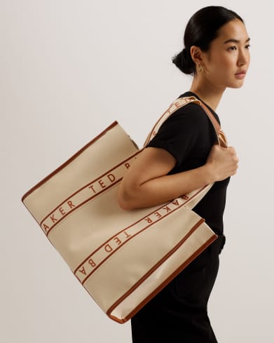 Woman in a black dress carrying cream tote bag