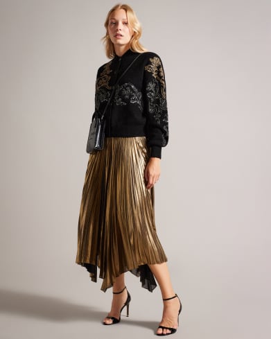 Woman in a gold embellished knit buttoned bomber with a gold skirt