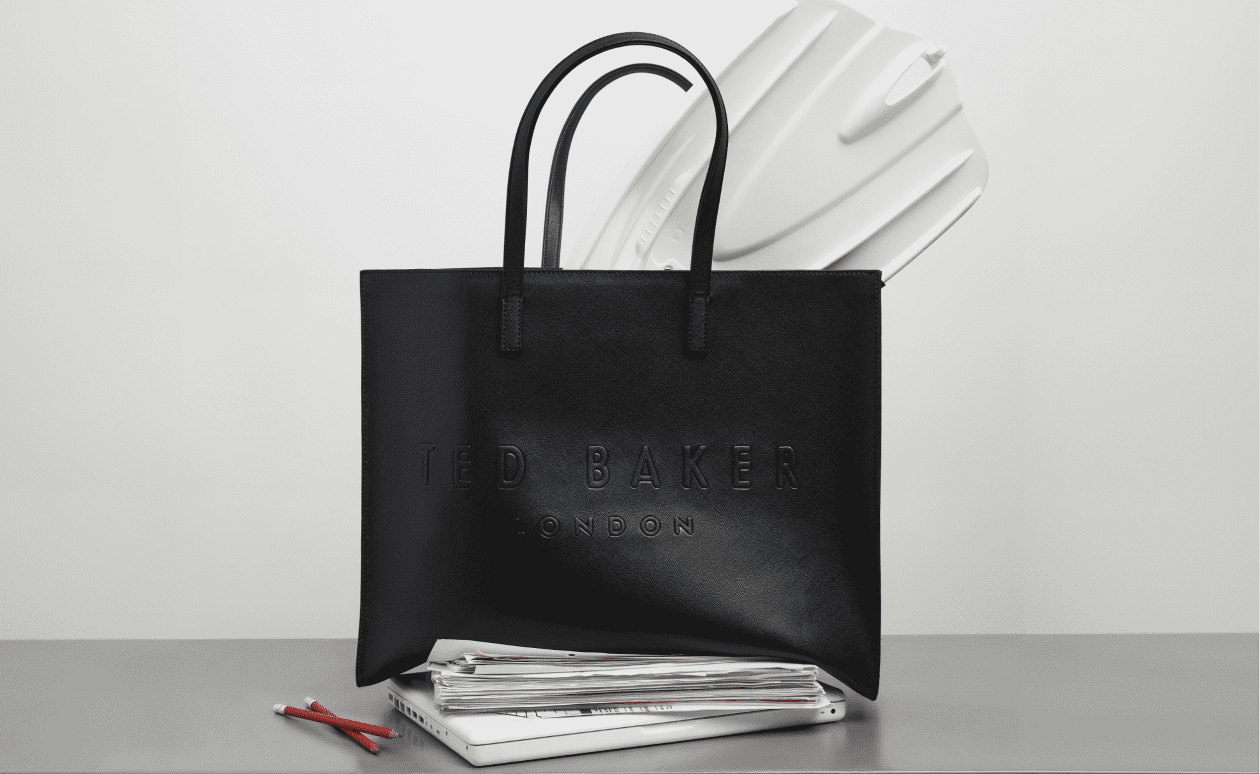 Women's black tote bag on a desk with paperwork underneath and with a white flipper coming out of it