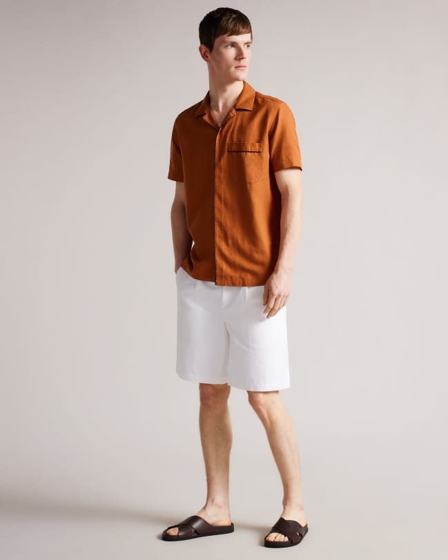 Man in burnt orange shirt wearing white shorts and brown leather sandals