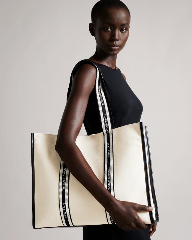 Woman in a black dress carrying a white large canvas tote bag with Ted Baker logo webbing