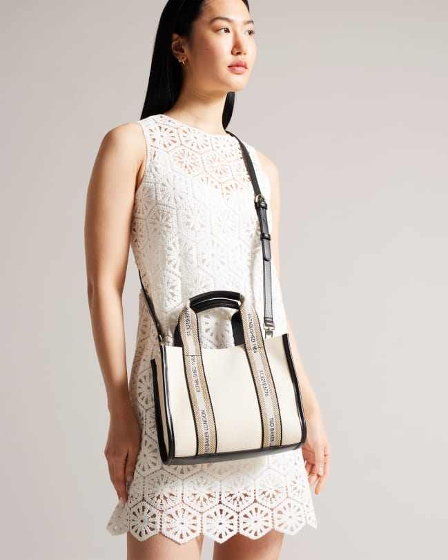 Woman in a white dress carrying a small large canvas tote bag with Ted Baker logo webbing